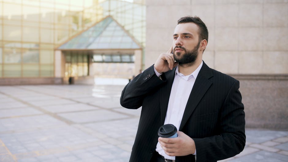 A professional businessman with a coffee cup makes a phone call outside a modern office building